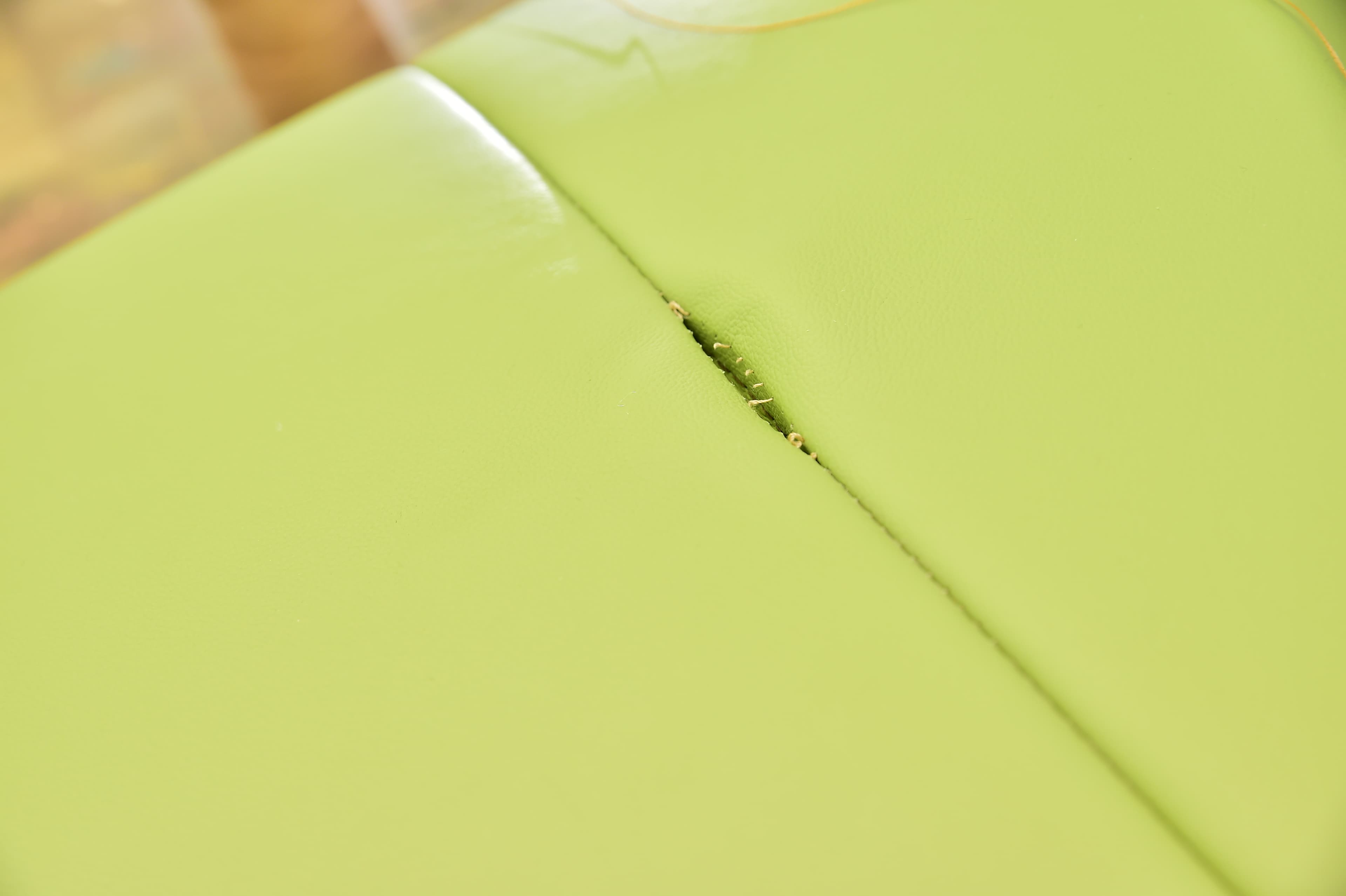 Gros plan d'un siège en vinyle vert clair avec une déchirure visible le long d'une couture, révélant le matériau en dessous.