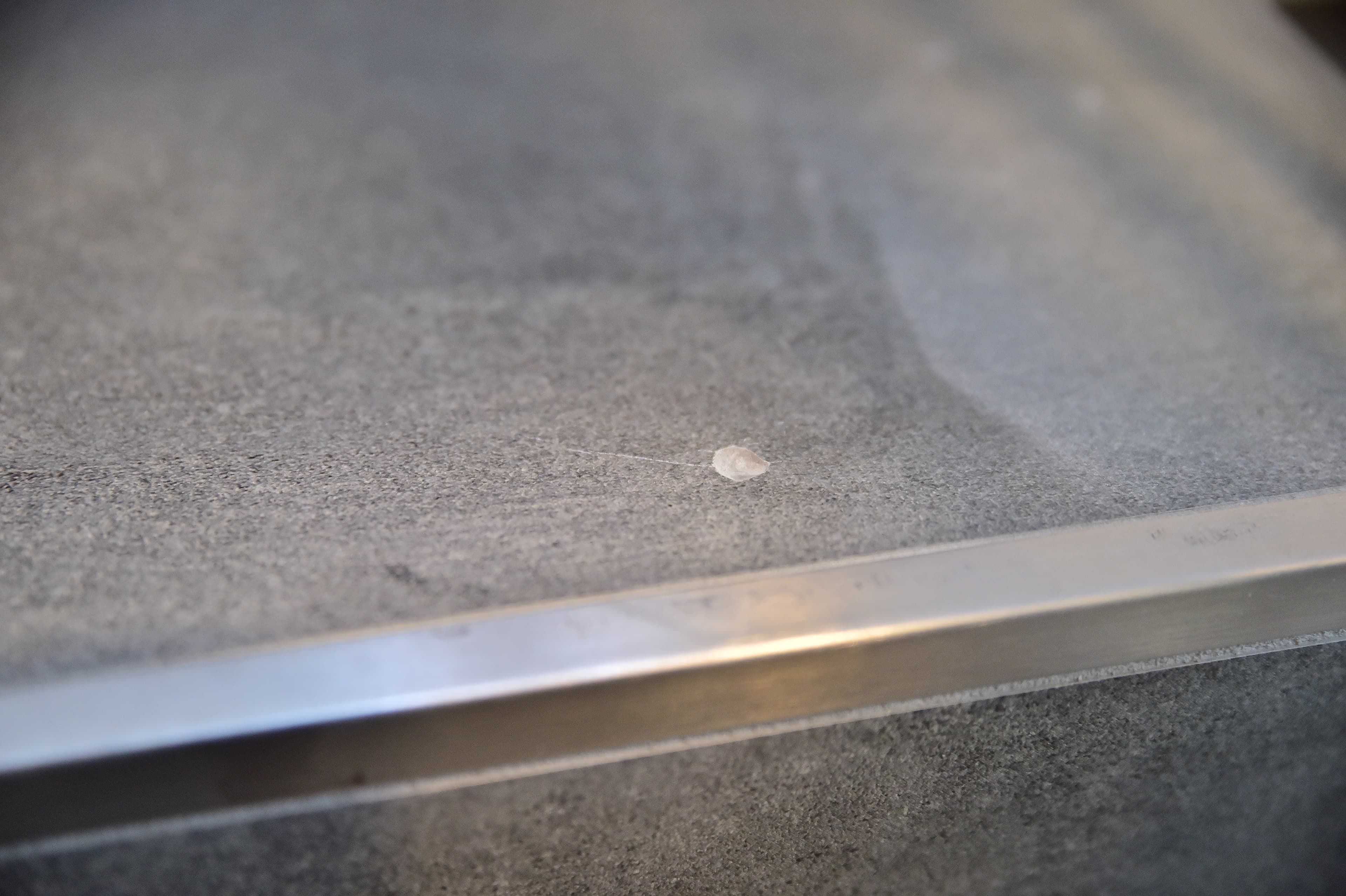 Ein kleines Stück Kaugummi klebt auf einer glatten, grauen Betonoberfläche in der Nähe einer Metallkante.