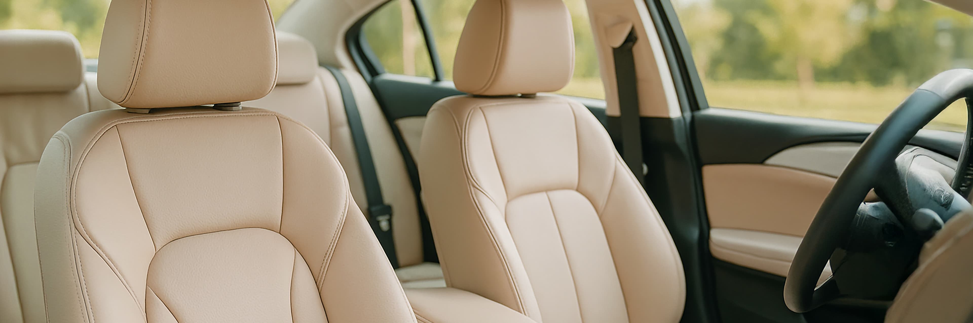 Zicht op het interieur van een auto met beige leren stoelen, een stuur aan de rechterkant en zonlicht door de ramen met een vaag groen landschap buiten.