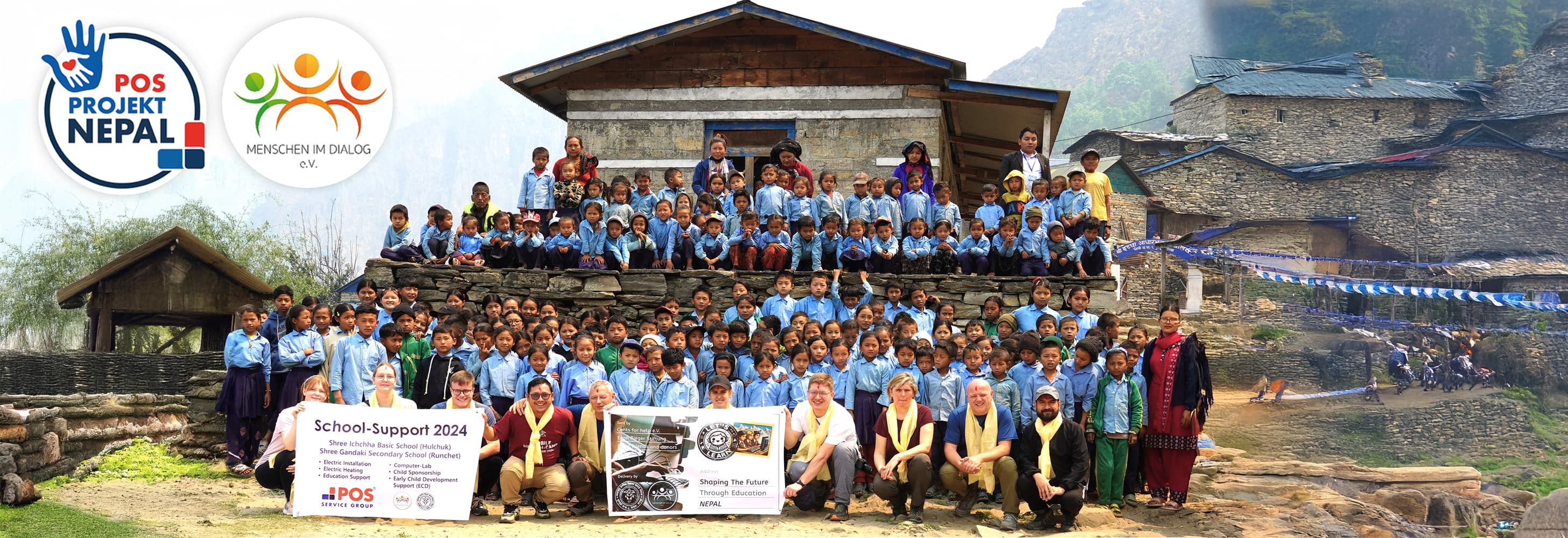 A large group of school children and adults pose outdoors in front of stone buildings and mountains, holding banners with logos for POS Projekt Nepal and MENSCH IM DIALOG e.V. and signs for school support 2024.