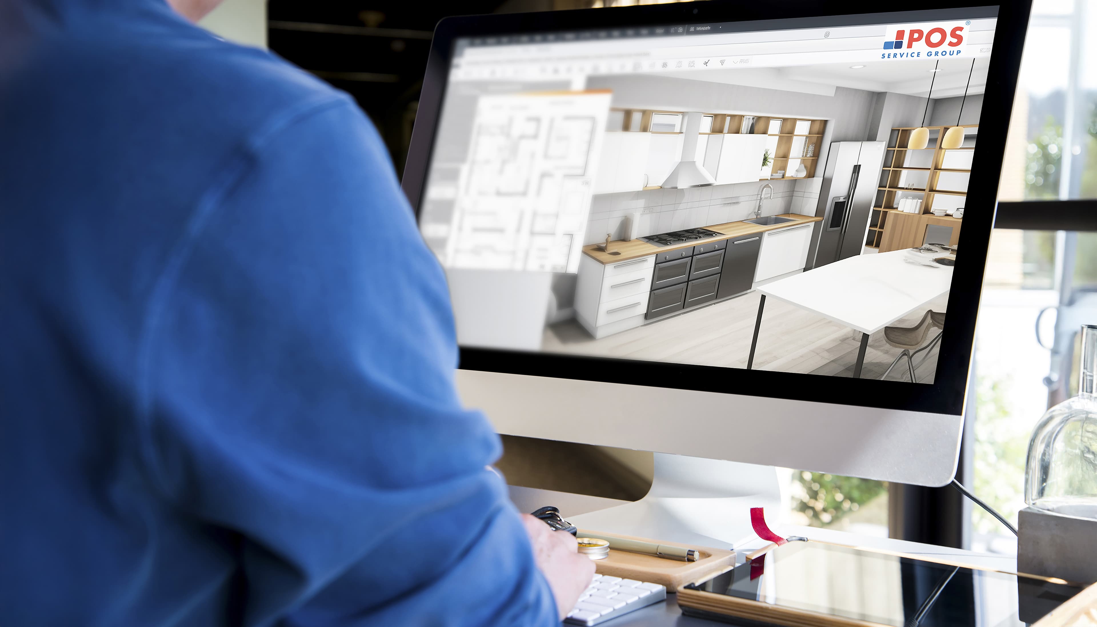Eine Person in einem blauen Hemd arbeitet an einem Desktop-Computer, der einen 3D-Küchenentwurf und einen Grundriss auf dem Bildschirm anzeigt, wobei das Logo der POS Service Group oben rechts zu sehen ist.
